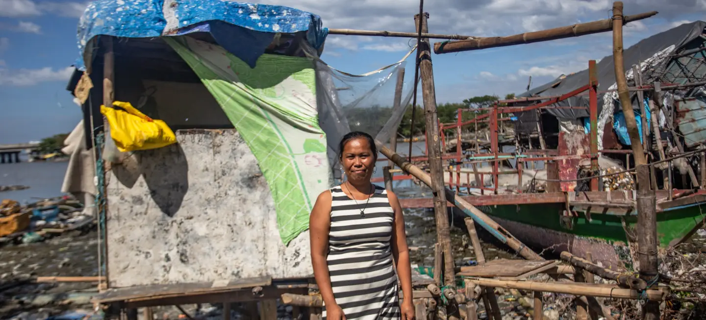 Portrait of Laarni Villamon with a dilapidated shelter and an out-of-commission boat in the background