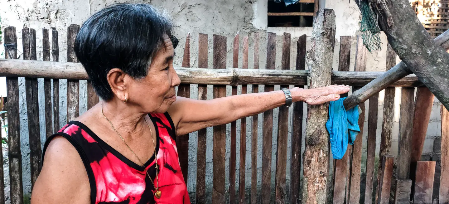 An elderly woman holding her hand against the fence showing the height reached by floodwaters in 2023